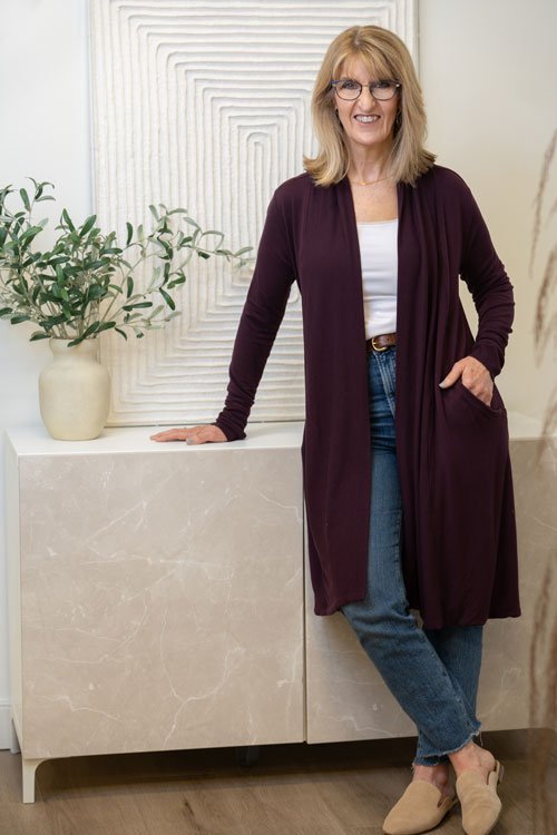 Martha leaning against an end table wearing a long dark-colored cardigan with one hand in her pocket.